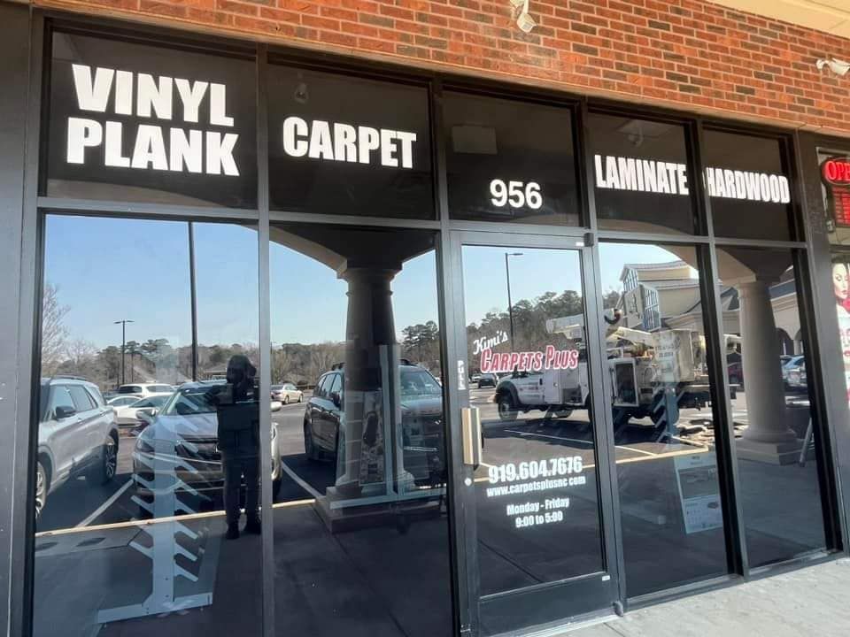 Storefront for a flooring business advertising vinyl plank, carpet, and laminate, located at unit 956 in a shopping center.