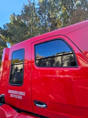 A bright red truck cab exterior with two dark-tinted windows, a silver door handle, and text printed on the side panel.
