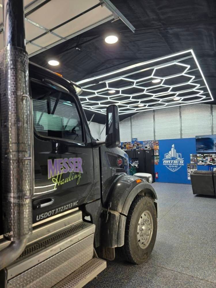A black Messer Hauling semi-truck parked in a garage with a decorative honeycomb LED ceiling light display.