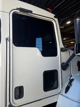 A white heavy-duty truck door showing a main window, a smaller lower peephole window, and an exterior door handle.