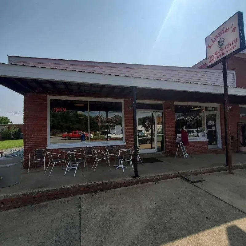A brick restaurant storefront, Lizzie’s Grill and Chill, with outdoor seating under a metal awning on a sunny day.