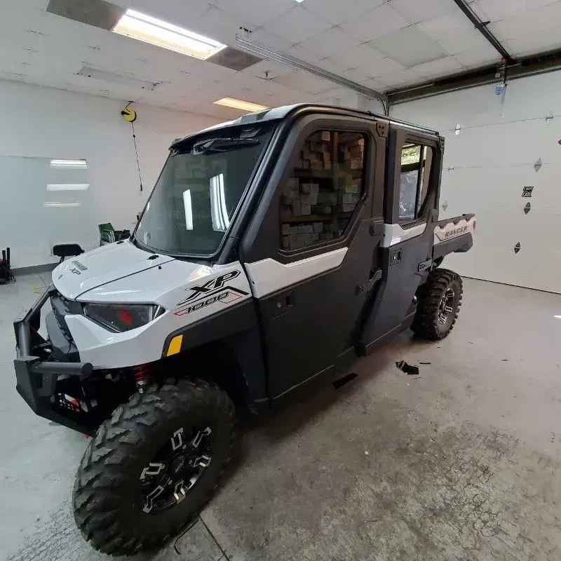 A white and black four-door Polaris Ranger UTV parked inside a garage.