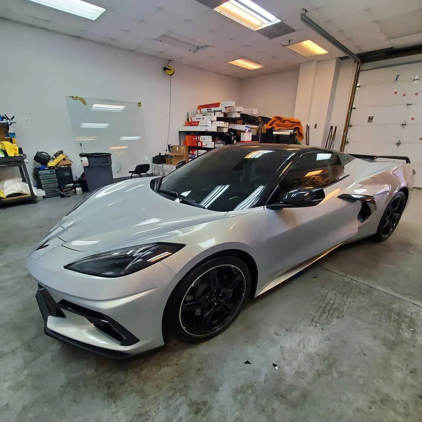 A silver Chevrolet Corvette sports car with a black roof and black wheels parked inside a garage.