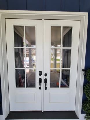 A pair of white French doors with glass panes and black hardware, set against a dark blue exterior wall.
