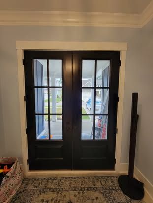 A pair of dark-stained wooden French doors with glass panes and white trim, viewed from inside a room with a rug.
