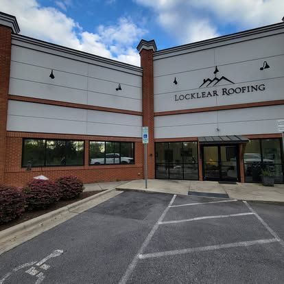 A brick building with white panels, a Locklear Roofing sign, and a parking lot with a handicapped space in the foreground.