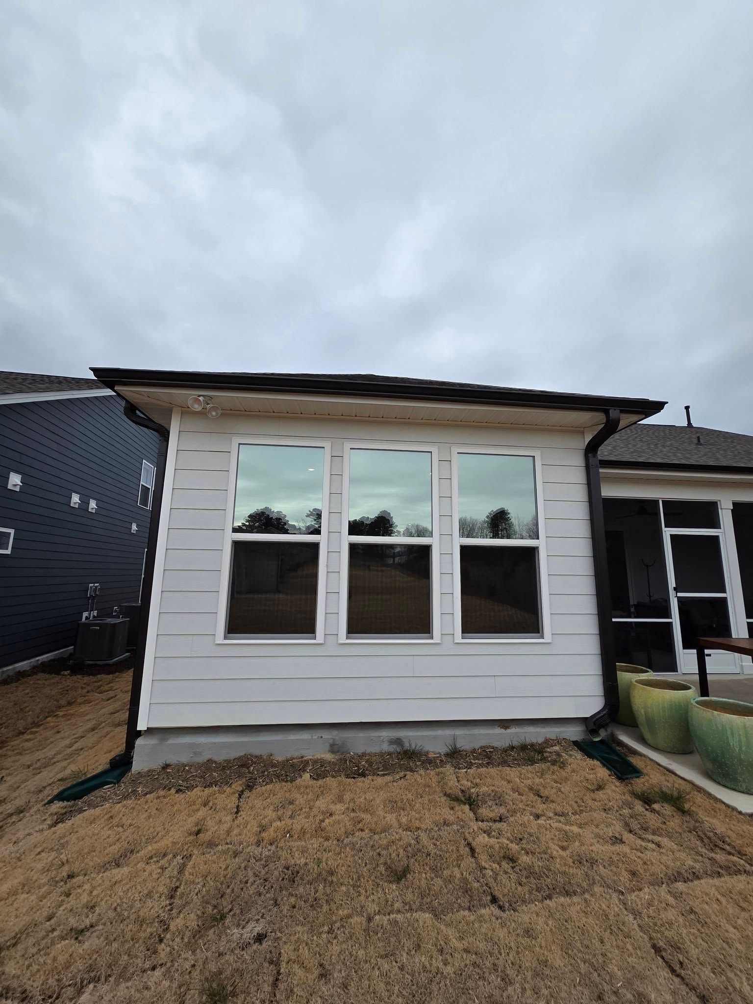 A light-colored house extension featuring three tall windows under a dark roof, set against a cloudy sky.