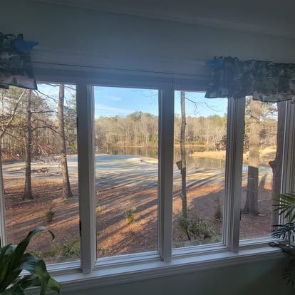 A window view of a sunny, tree-lined landscape with a small body of water in the distance.