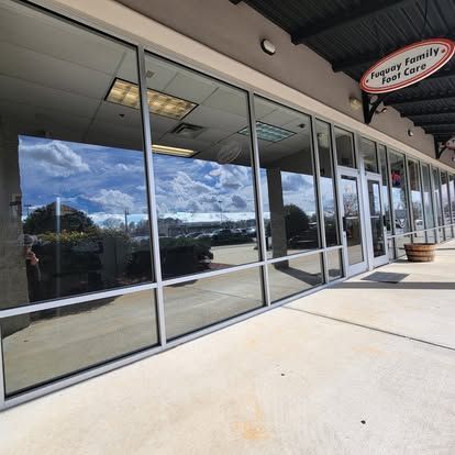 The storefront of Fuquay Family Foot Care, featuring a large glass window reflecting the sky and a nearby parking lot.
