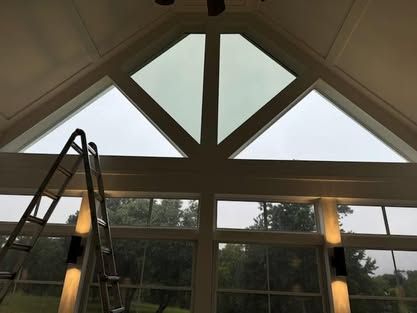 A tall metal ladder positioned against a set of large, multi-paned windows in a room with a peaked ceiling.