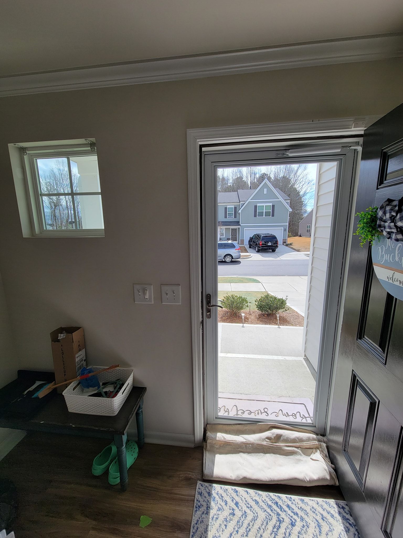 An indoor view from an entryway showing a front door, a side window, an entry table with items, and a mat on the floor.