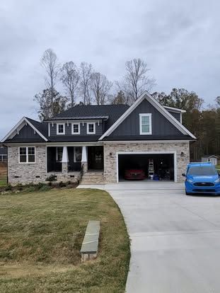 A suburban home with light brick, dark grey gabled roof, and white accents, featuring a two-car garage and a blue van.