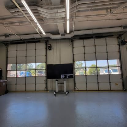 A large television screen on a rolling stand positioned between two industrial garage doors in a bright workshop.