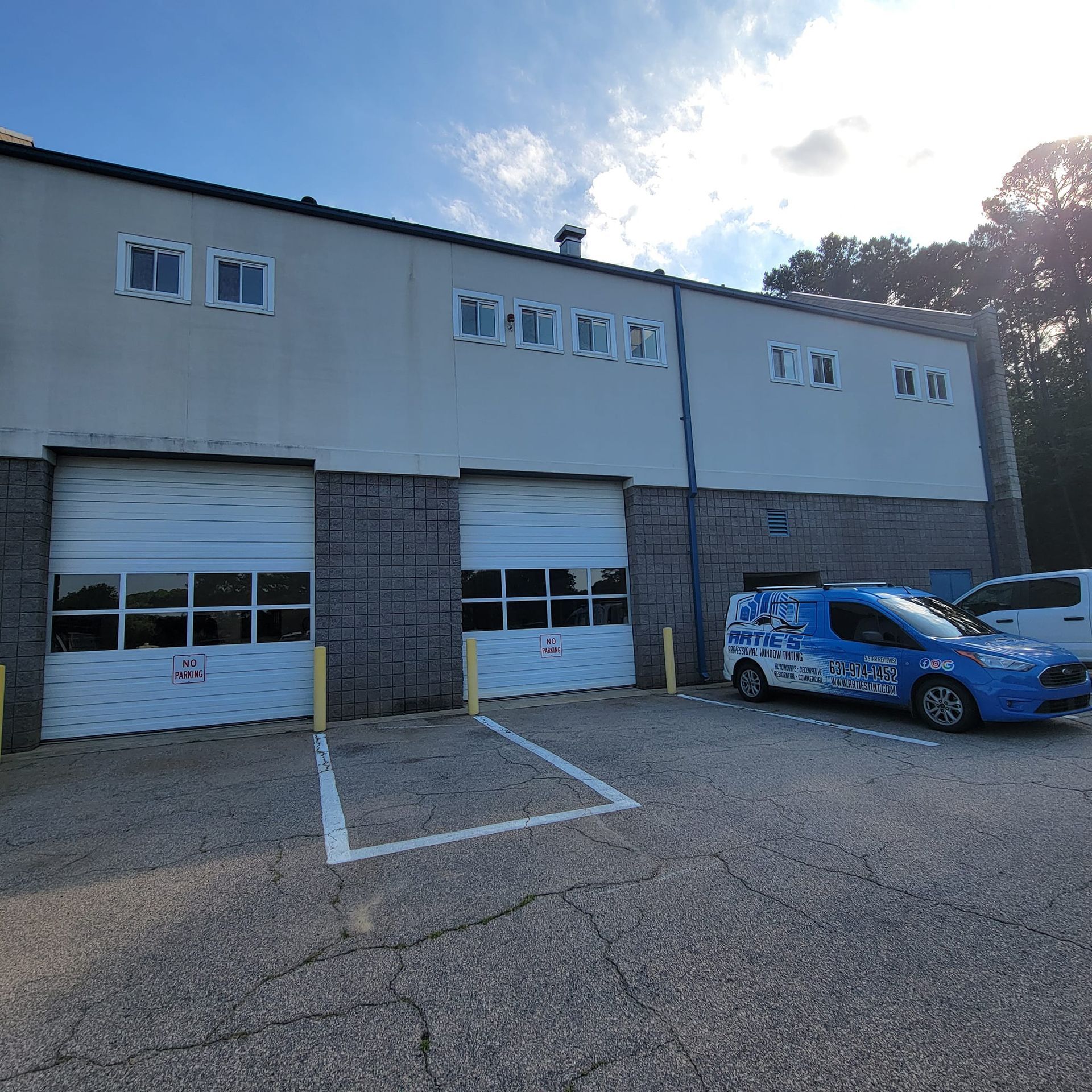 A blue service van parked in front of a two-story commercial building with two closed white roll-up garage doors.
