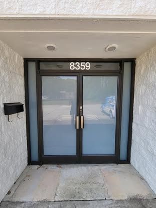 Double glass front doors labeled with address number 8359, set in a white textured wall with a black mailbox.