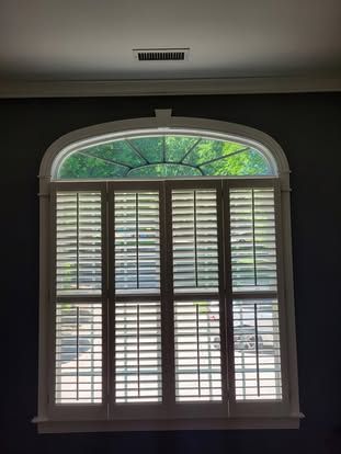 Arched window with white plantation shutters against dark grey walls.