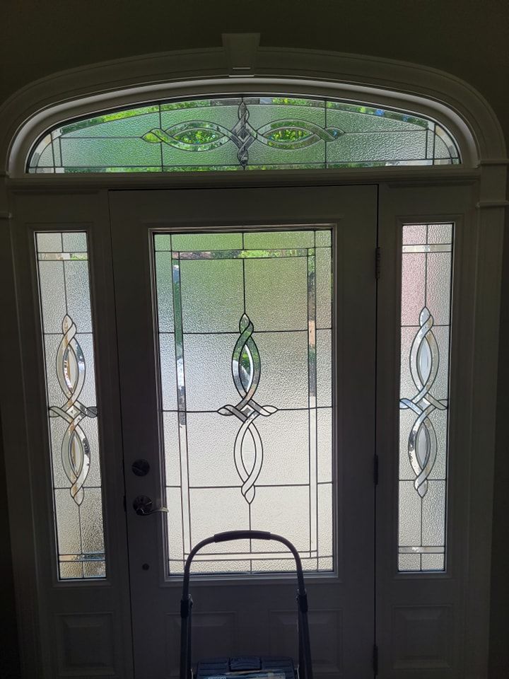 A white arched front door with decorative leaded glass panels and a matching transom window above, seen from indoors.