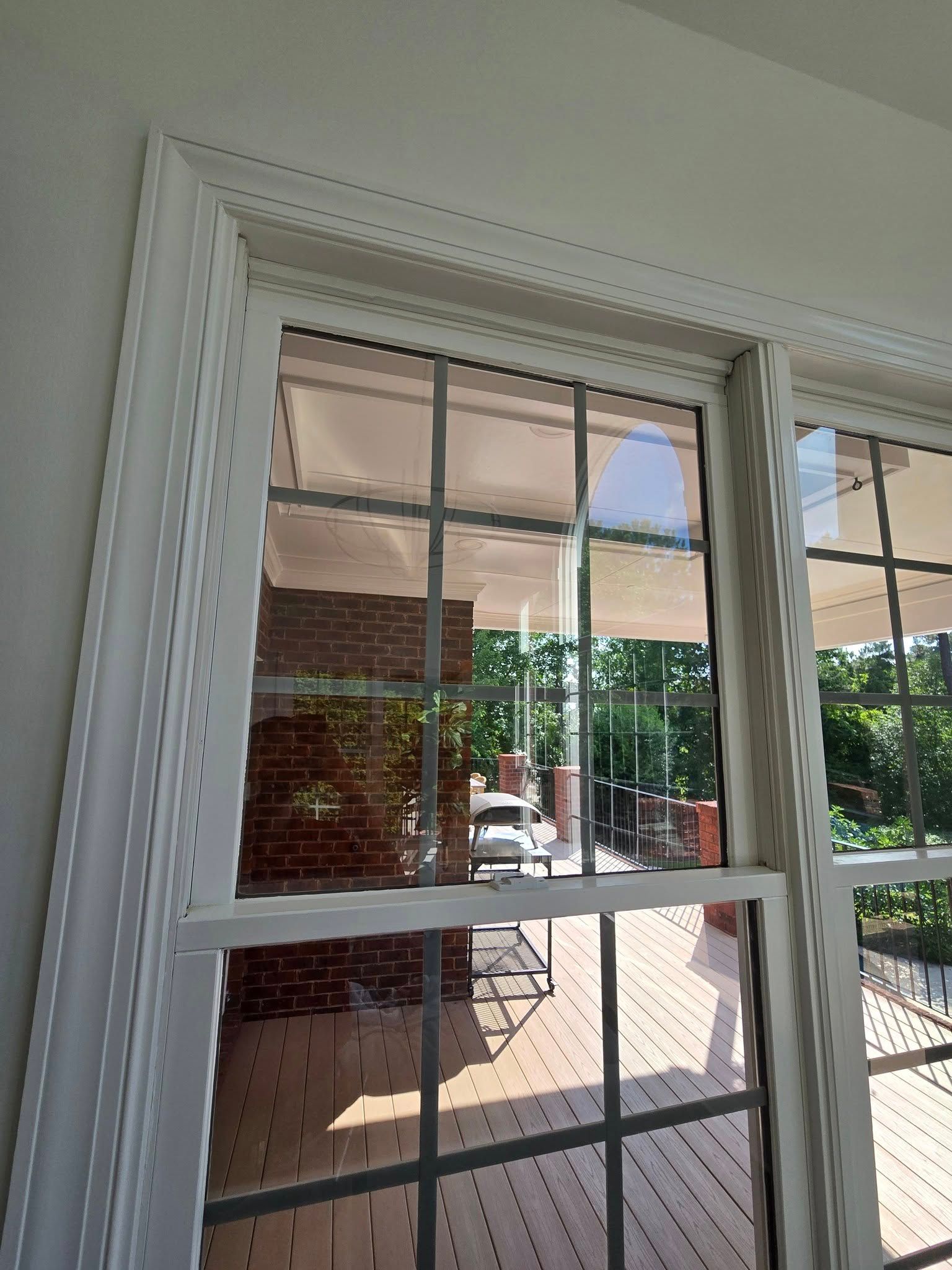 A white, multi-pane window frame viewed from inside, looking out at a brick porch and outdoor greenery.