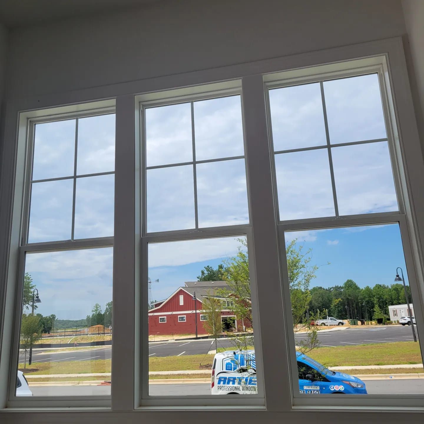 Three white-framed, double-hung windows with grid patterns installed in a wall with beige horizontal siding and green trim.
