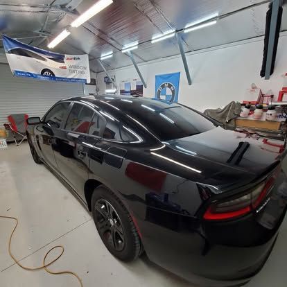 A black Dodge Charger parked inside a well-lit garage, viewed from the rear passenger side angle.