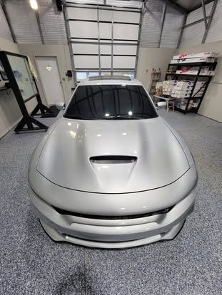 A silver Dodge Charger parked in a bright, modern garage with gray epoxy flooring and a metal roll-up door in the back.