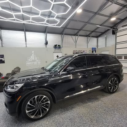 A black luxury SUV parked inside a modern automotive detail shop with bright, geometric LED lighting on the ceiling.