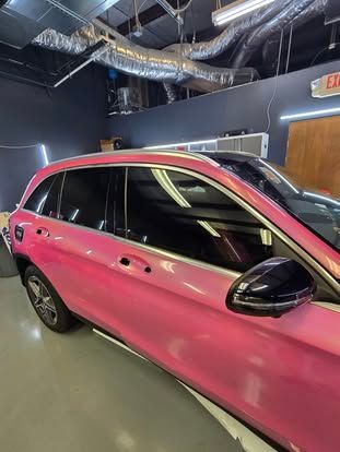 A bright pink SUV parked inside a garage with exposed industrial ceiling pipes and a light-colored floor.