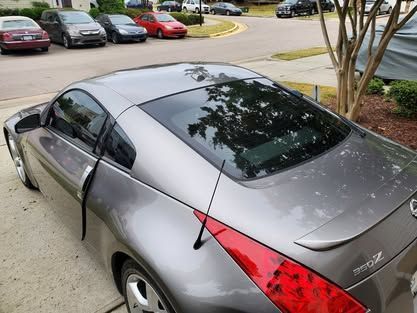 High-angle shot of a gray Nissan 350Z parked in a driveway, showing exterior paint wear and a detached rubber door seal.