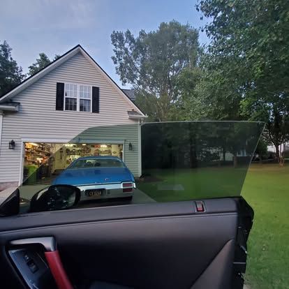 A view from inside a car looking out at a blue vintage car parked in a garage at sunset.