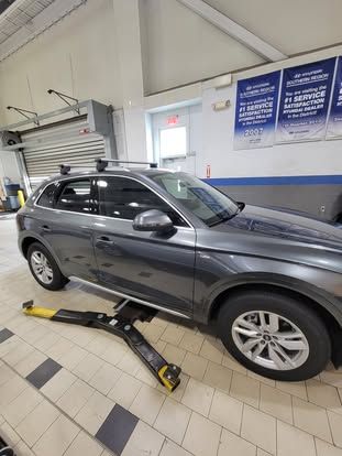 A dark gray SUV parked inside a service garage with a hydraulic lift arm positioned underneath it.