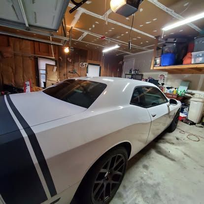 A white Dodge Challenger with black racing stripes parked inside a garage.
