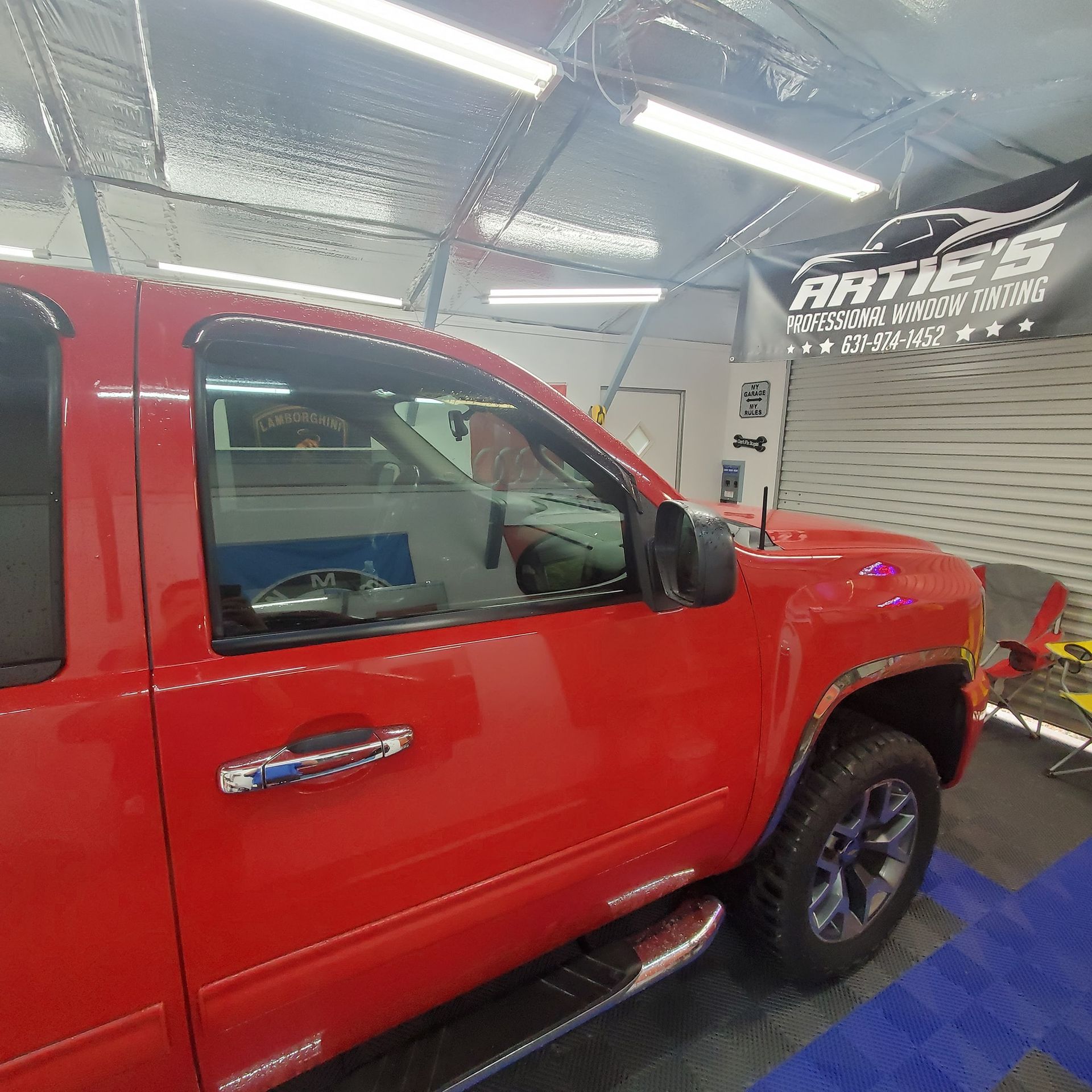Side view of a bright red pickup truck inside a professional window tinting garage with an 