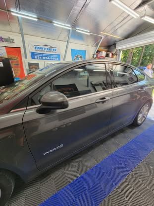 A grey sedan sits inside a garage with bright lights, a blue floor mat, and wall posters.