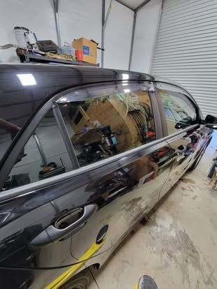 Black car parked in a garage, focusing on the windows, door handles, and newly installed rain guards.