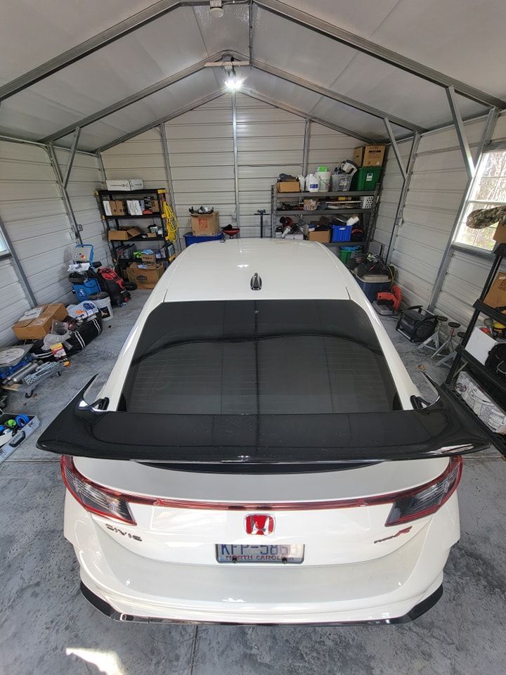A white Honda Civic Type R with a black spoiler parked inside a well-lit, cluttered metal garage.