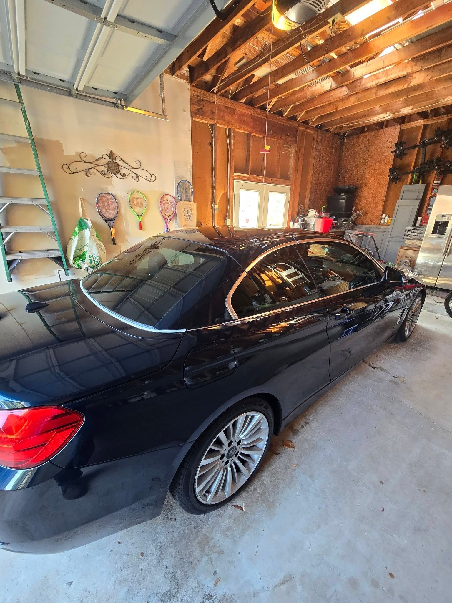 A glossy black sedan parked inside a garage with wooden ceiling beams and a ladder leaning against the wall.