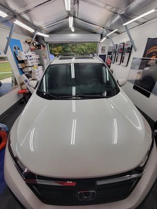 A white Honda car parked inside a well-lit workshop with shelves and signs on the walls.