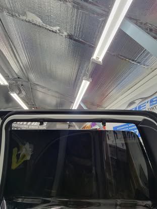 An interior view of a vehicle door frame with a dark tinted window and rubber weather stripping against a reflective ceiling.