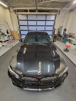 A dark-colored BMW parked in the center of a well-lit, professional automotive garage.