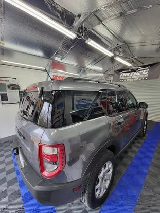 A gray SUV parked in a well-lit indoor garage with a tiled floor and overhead fluorescent lights.