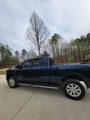 A dark blue crew cab pickup truck parked on a concrete driveway with trees in the background.