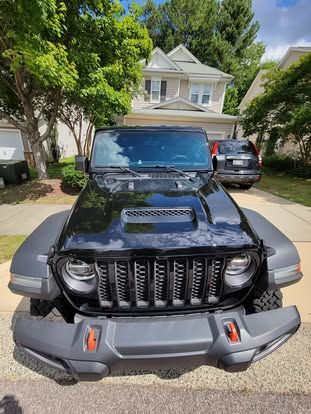 A black Jeep Wrangler with a vented hood parked in a residential driveway on a sunny day.