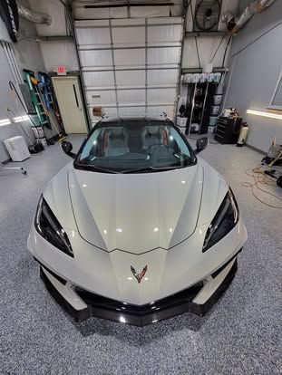 A high-angle view of a white Chevrolet Corvette parked in a clean, brightly lit professional garage.