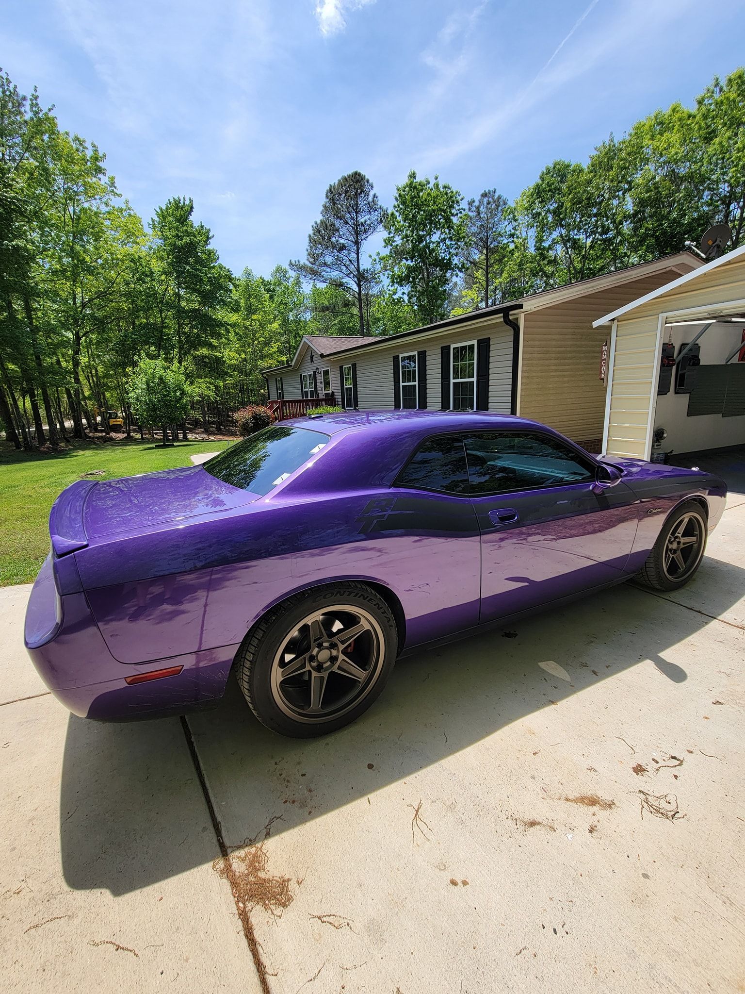 A bright purple Dodge Challenger parked on a concrete driveway in front of a house on a sunny day.