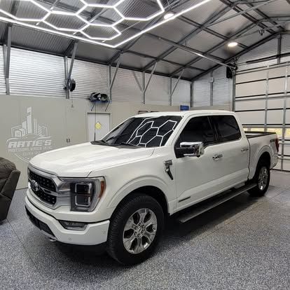A white Ford F-150 pickup truck parked inside a modern garage with hexagon LED ceiling lights.