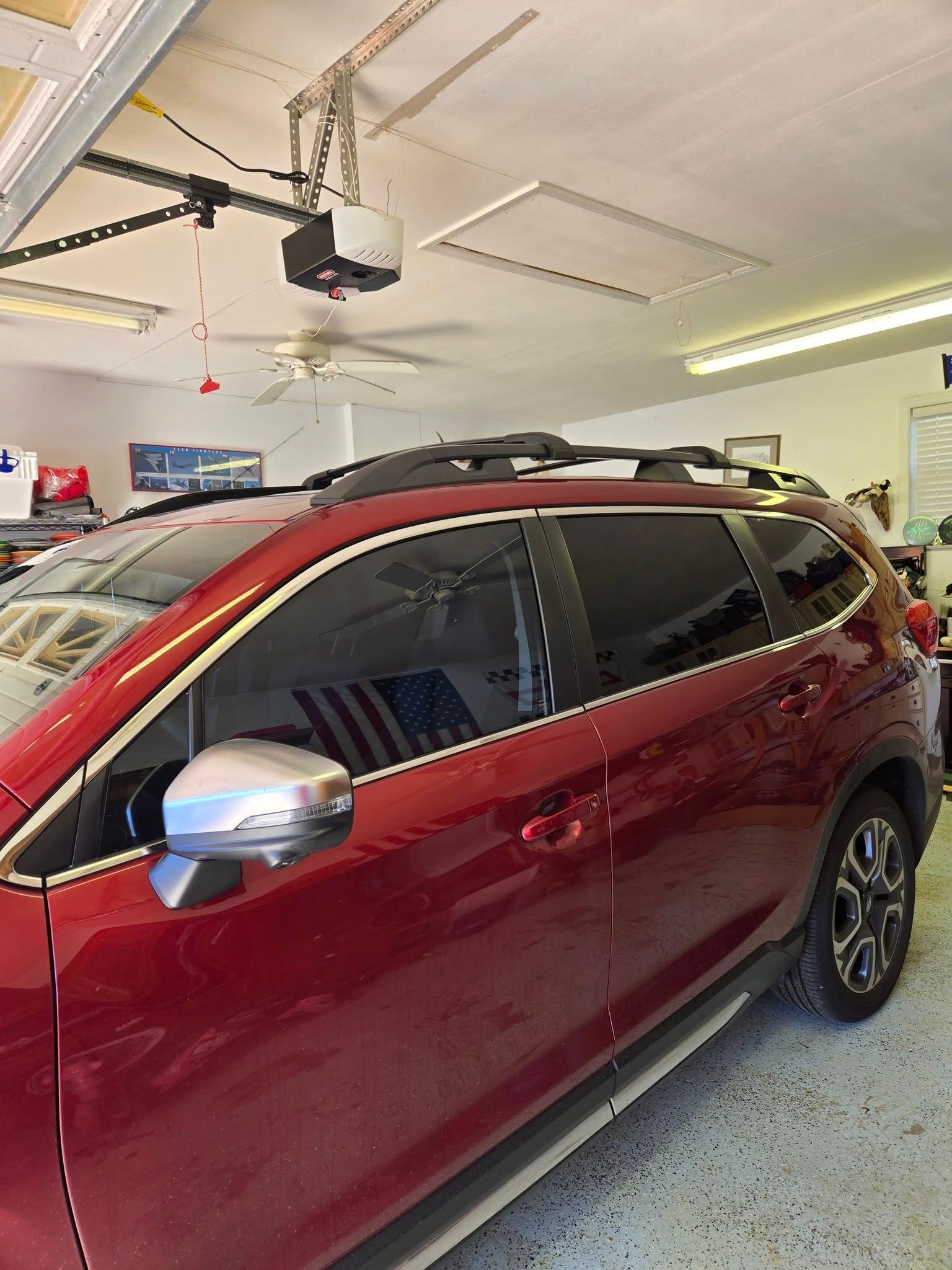 A maroon SUV parked inside a residential garage, showcasing side windows with dark tinting and a roof rack.