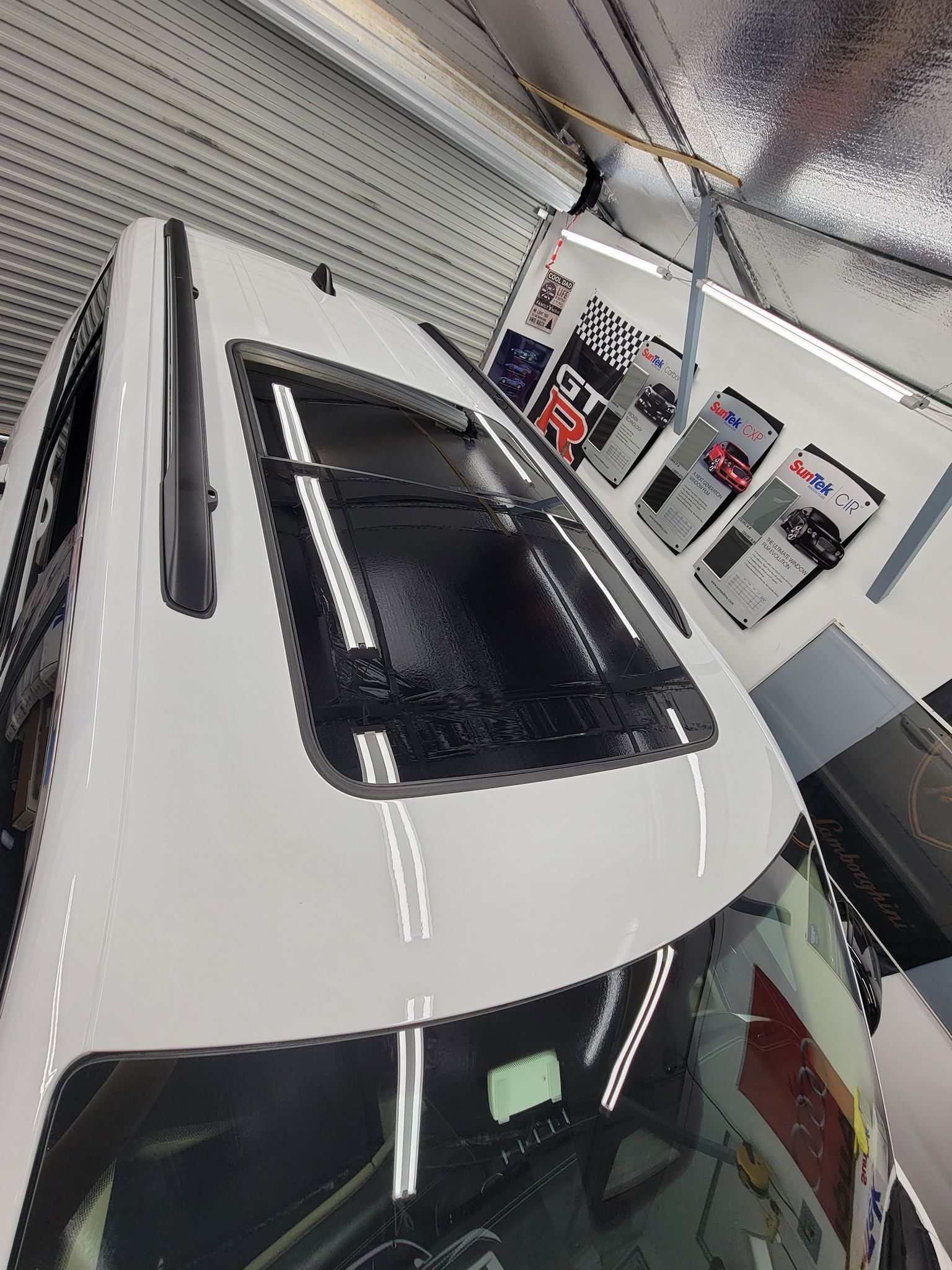A high-angle view of a white car roof featuring a panoramic sunroof, parked inside a brightly lit garage or workshop.