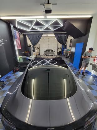 A high-angle view of a gray car inside a brightly lit professional detailing shop with checkered floors.