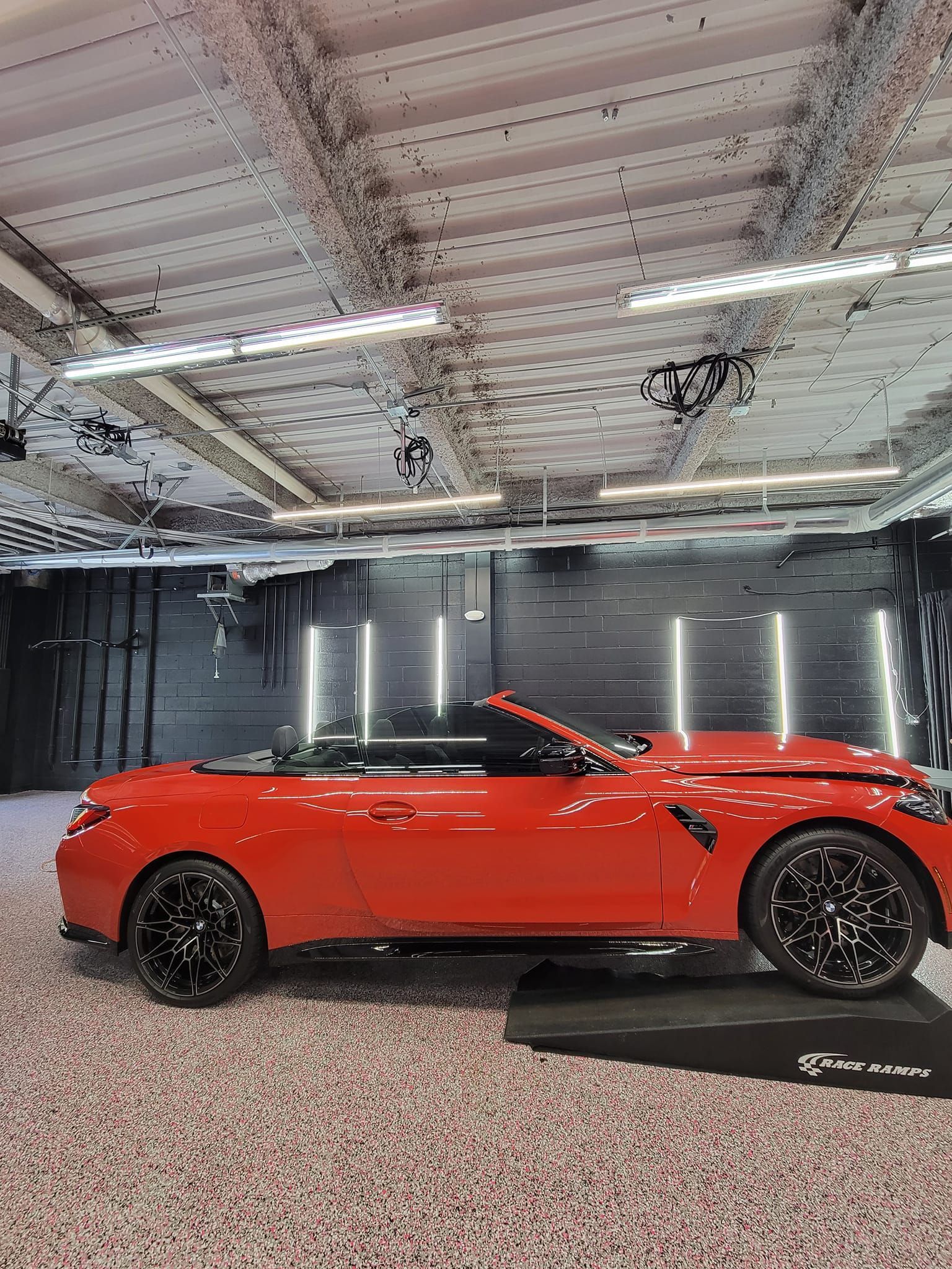 A bright orange BMW convertible displayed on a black platform inside a modern, industrial-style garage with LED lighting.