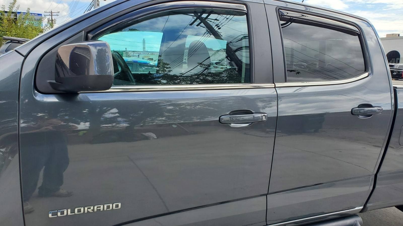 A close-up of the side profile of a grey Chevrolet Colorado truck, showing the front and rear doors and side mirrors.